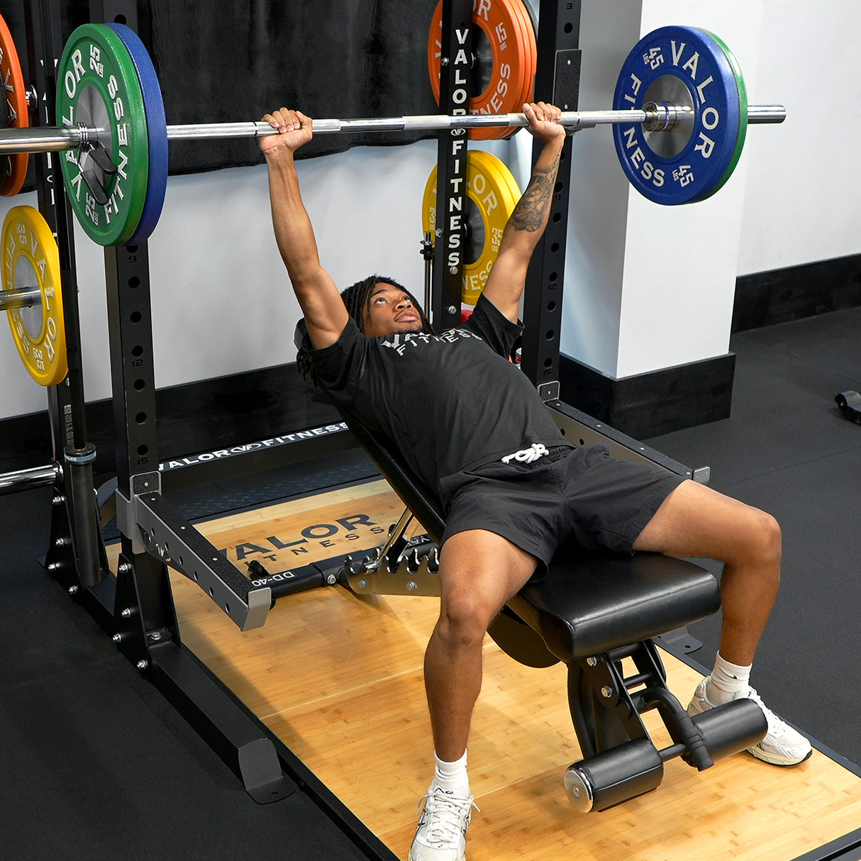 Incline bench presses with Valor Fitness barbell, adjustable bench, and half rack weightlifting platform