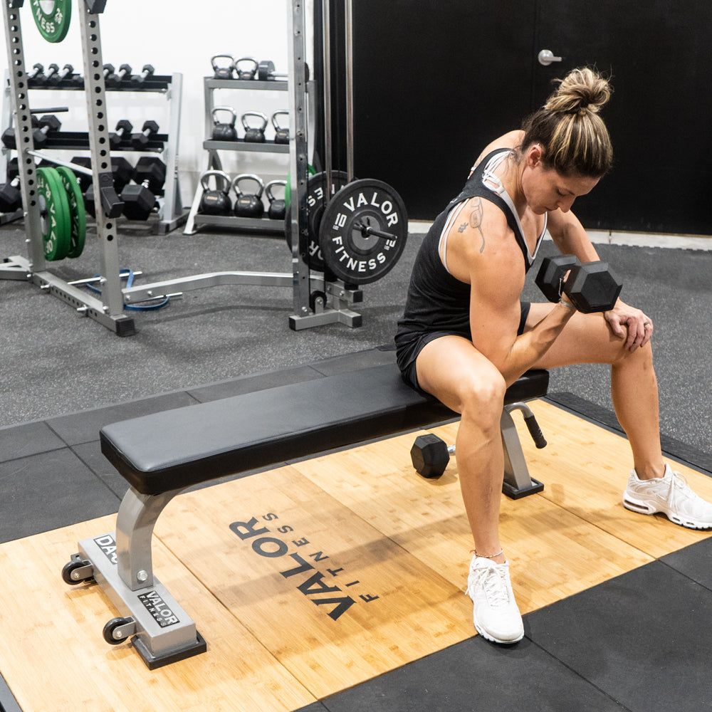 Woman doing dumbbell curls on a Valor Fitness flat weight bench