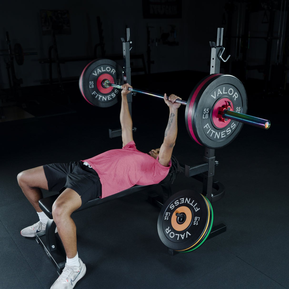 Person exercising a bench press with barbell and Valor Fitness weights in a gym setting