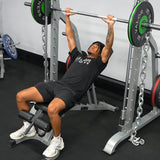 Person performing a bench press with Valor Fitness smith machine and weight plates in a gym setting